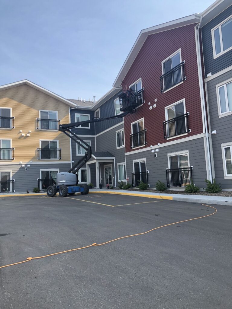 window cleaner working from a lift washing the third-storey windows on a commercial residential building for a cleaning company in Wainwright
